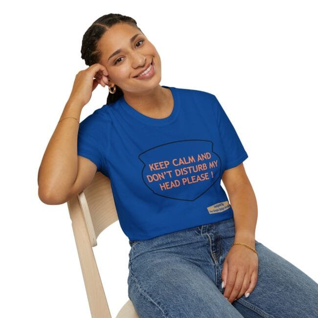 Woman sitting on a light wooden chair, smiling, wearing a blue T-shirt with the orange text: 'KEEP CALM AND DON'T DISTURB MY HEAD PLEASE!'