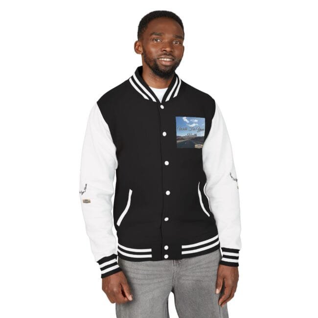 Man wearing a black and white varsity jacket with striped cuffs, standing and smiling toward the camera. A patch on the chest shows a scenic image.