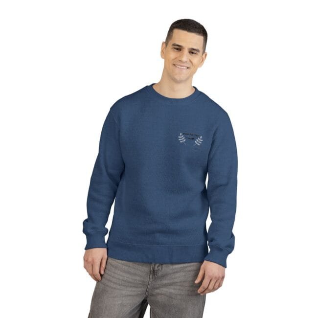 Man in a blue crewneck sweater with a small white embroidered leaf design on the left chest, standing casually and smiling.