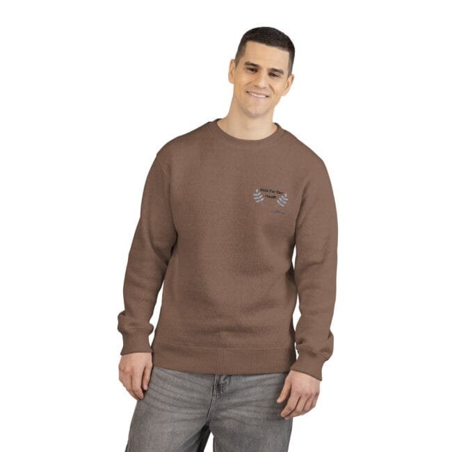 Smiling man wearing a brown crewneck sweatshirt with a small left-chest embroidery, standing against a white background.