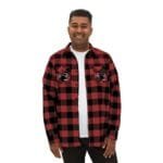 Man in a red and black plaid flannel shirt over a white T‑shirt, smiling at the camera.