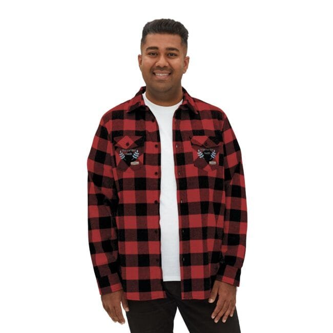 Man in a red and black plaid flannel shirt over a white T‑shirt, smiling at the camera.