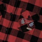 Close-up of a red and black plaid shirt pocket with embroidery reading 'Walk For Your Health' and blue leaves nearby.