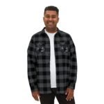 Man wearing a black and gray plaid flannel shirt over a white tee, smiling at the camera with embroidered patches on each chest pocket.
