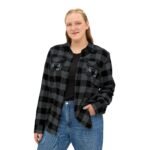 Woman wearing a black-and-gray plaid flannel shirt with embroidered patches on the chest pockets, posing with one hand in her pocket.