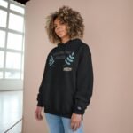 Young woman with curly hair wearing a black hoodie featuring 'Walk For Your Health' and blue leaf graphics, standing against a peach wall in a bright room.