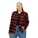 Young woman in a red and black plaid flannel shirt with pockets, smiling softly, hands in pockets.