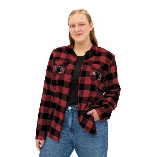 Young woman in a red and black plaid flannel shirt with pockets, smiling softly, hands in pockets.