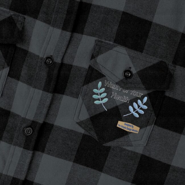 Close-up of a dark gray plaid shirt pocket with embroidery: 'Walk For Your Health' and blue leaf accents.