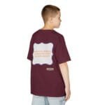 Back view of a boy wearing a maroon oversized T-shirt with a white decorative patch on the back containing orange text: 'CONTINUOUS LEARNING IS IMPROVING YOUR CULTURE'S MINDSET'.