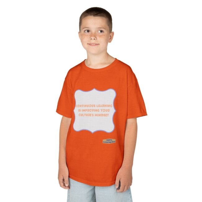Boy with short hair and freckles wearing an orange T-shirt that features a white framed panel with the message about continuous learning when read up close.