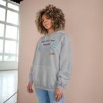 Young woman wearing a gray hoodie with 'Walk For Your Health' and teal leaf graphics, standing against a peach wall.