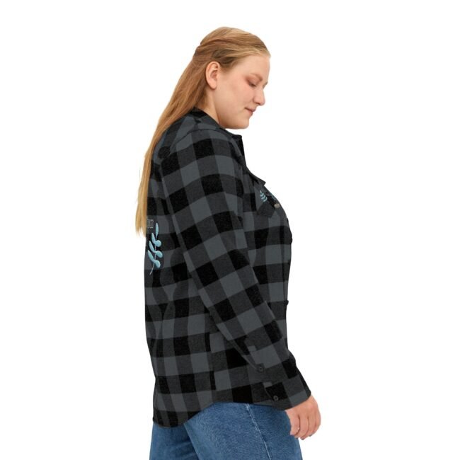 Side view of a woman wearing a black and gray plaid flannel shirt with blue floral embroidery on the back, paired with blue jeans