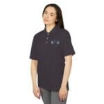 Woman wearing a dark polo shirt with short sleeves, featuring light blue embroidered laurel wreath and a small badge on the chest.