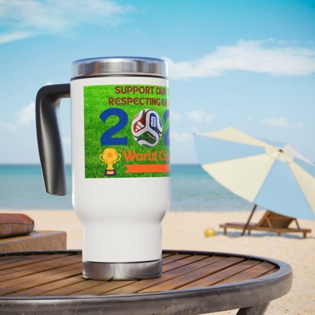 Close-up of a white mug with a bright green World Cup sticker and soccer ball artwork, placed on a wooden table at the beach