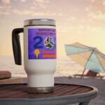 White travel mug with a purple World Cup sticker on a wooden table at the beach, with umbrellas in the background