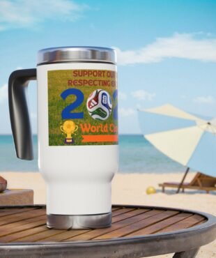 White mug on a wooden table at the beach with a colorful World Cup sticker featuring a soccer ball and trophy image