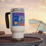 White mug with a colorful World Cup graphic and a black handle, placed on a wooden beachside table at sunset.