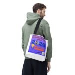 Side-profile of a man in an olive-green hoodie carrying a white tote bag with a purple poster showing a World Cup design