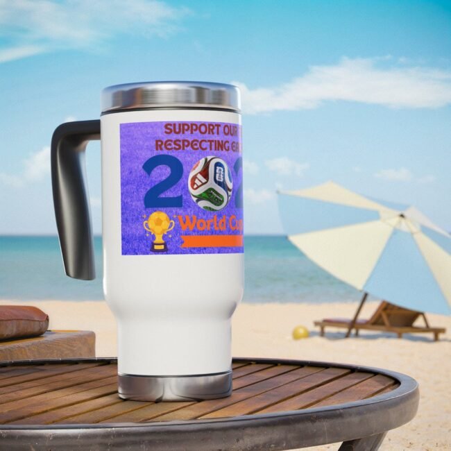 White travel mug with a purple World Cup sticker and soccer ball graphic on a wooden table at the beach
