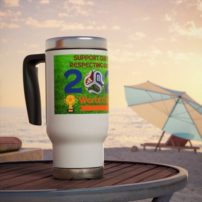Close-up of a white mug with a green World Cup label on a wooden table at the beach, with umbrellas in the background at sunset.