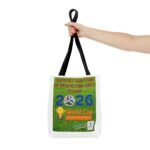 Close-up of a hand gripping a black tote bag strap; the bag displays a green poster with the message “Support Our Team by Respecting Each Other.”