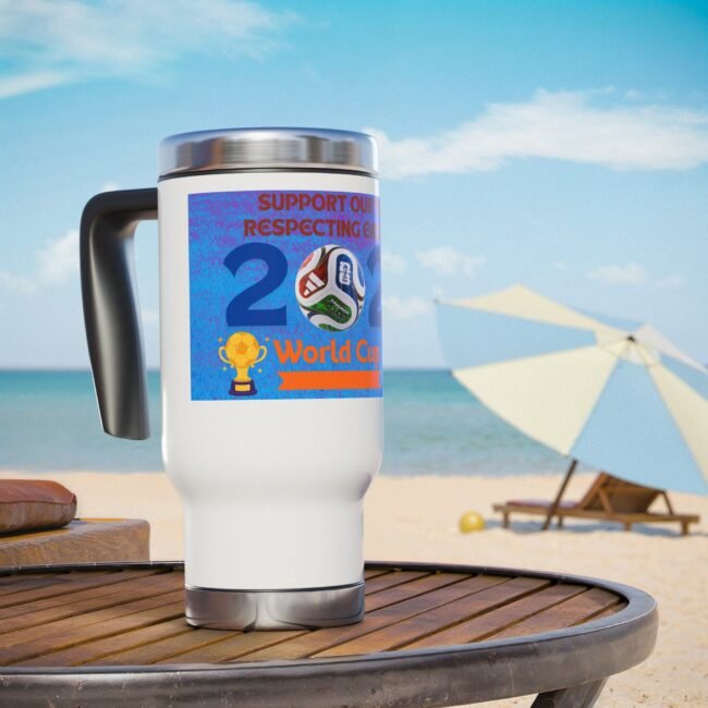 White insulated mug with a blue World Cup sticker on a beach table, ocean in the background.